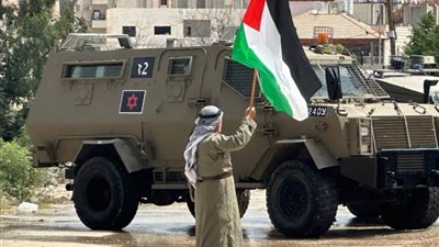 مسنٌ فلسطينيٌ يرفع العلم الفلسطيني عاليًا فوق مظاهر التدمير في طولكرم