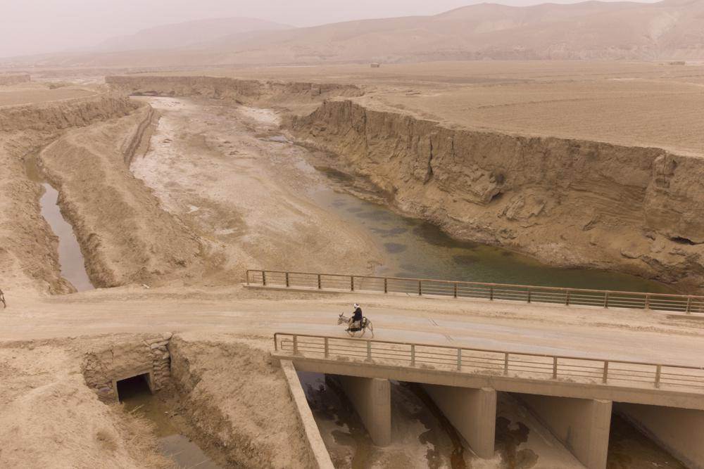 مزارع أفغاني يستخدم حمارًا لنقل عبوات المياه عبر النهر الجاف بالقرب من سانغ إي أتاش ، أفغانستان